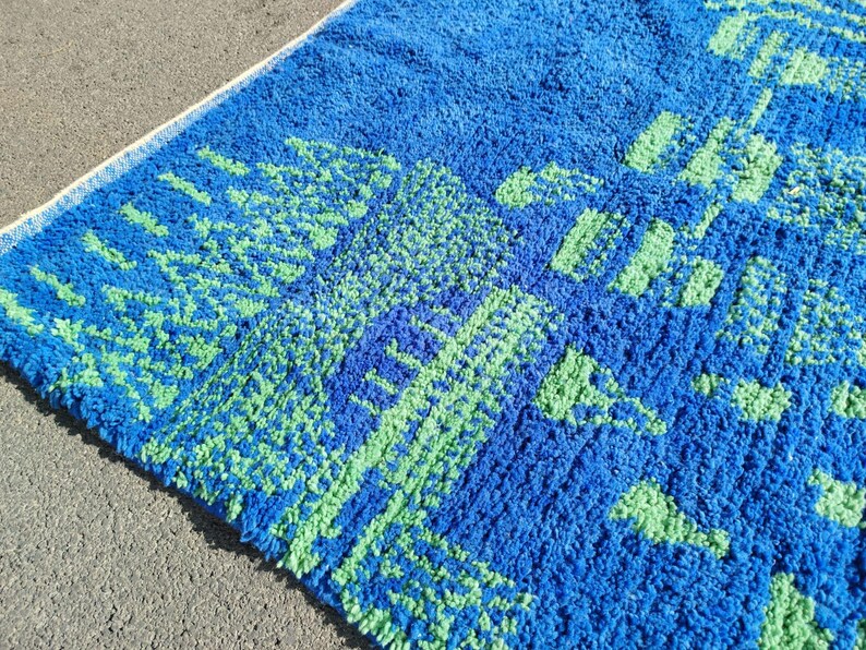 May include: Blue and green bath mat with a geometric pattern. The mat has a fluffy texture.
