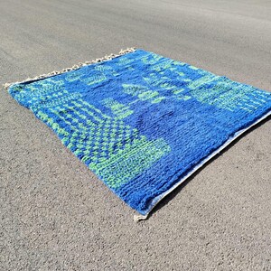 May include: A blue and green patterned rug with a fringed edge. The rug has a geometric design with a blue background and green accents.