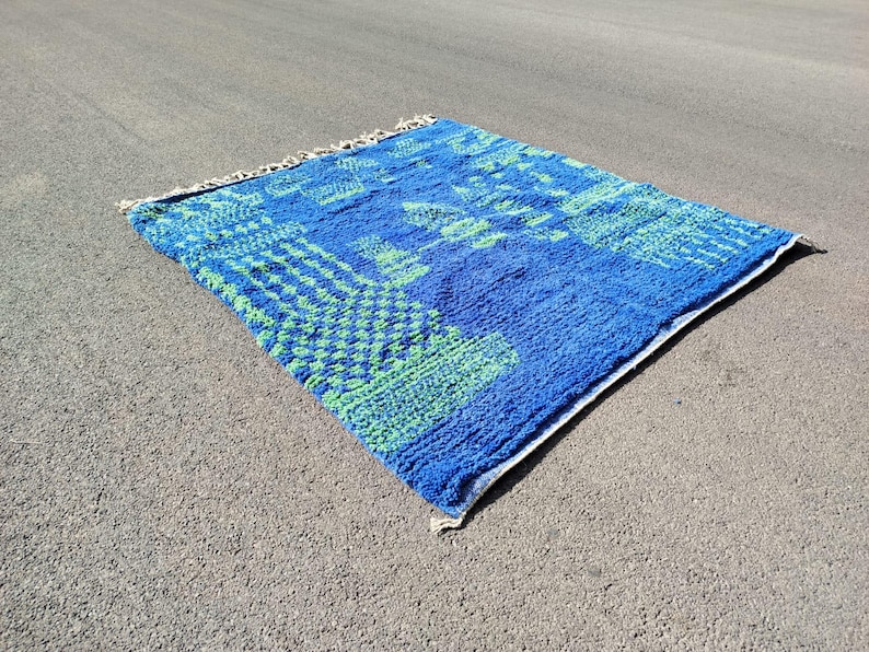 May include: A blue and green patterned rug with a fringed edge. The rug has a geometric design with a blue background and green accents.