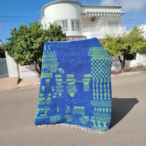 May include: A blue and green patterned rug with a geometric design. The rug is made of wool and has a fringe border.