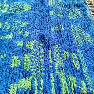 May include: A blue and green patterned rug with a fringe border. The rug is made of a soft, fluffy material.