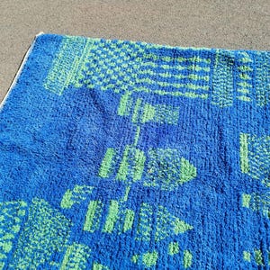 May include: A blue bath mat with a green geometric pattern. The mat is made of a soft, fluffy material.