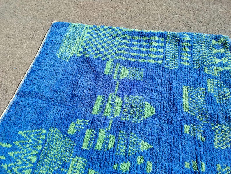 May include: A blue bath mat with a green geometric pattern. The mat is made of a soft, fluffy material.