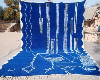 Puede incluir: Una alfombra marroquí azul y blanca con un patrón geométrico. La alfombra está tejida a mano y tiene un borde de flecos.