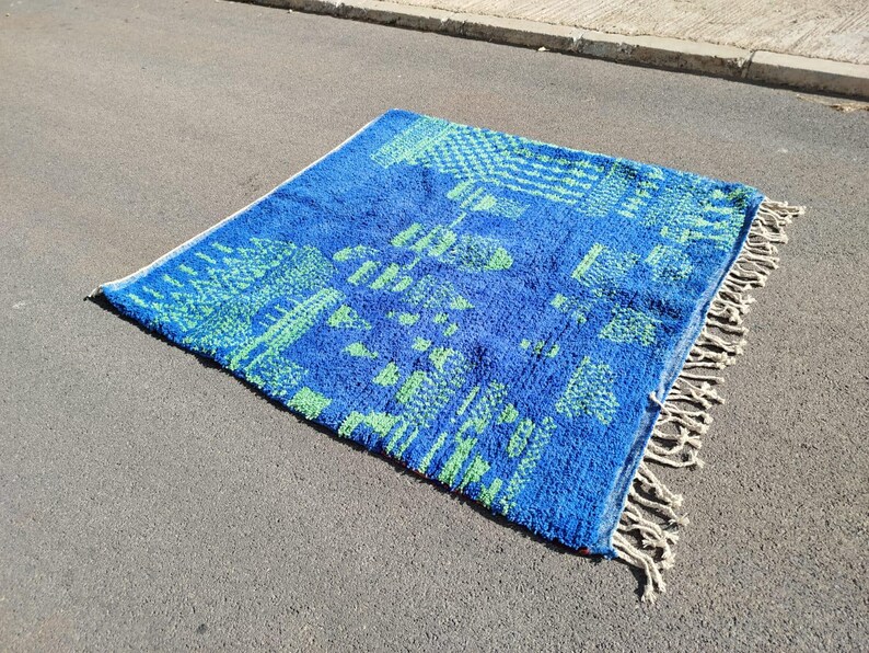 May include: A blue and green patterned rug with white fringe. The rug has a geometric design with a Moroccan style.