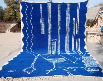 Puede incluir: Una alfombra marroquí azul y blanca con un patrón geométrico. La alfombra está hecha de lana y tiene un borde de flecos.