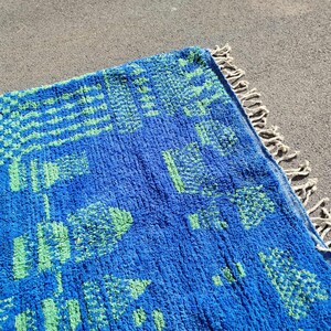 May include: A blue and green patterned rug with a fringe border. The rug has a geometric design with squares and rectangles.