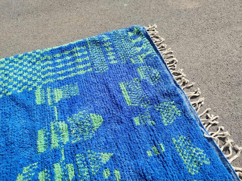 May include: A blue and green patterned rug with a fringe border. The rug has a geometric design with squares and rectangles.