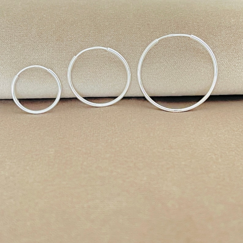 May include: Three silver hoop earrings of different sizes. The earrings are arranged in order of size, with the smallest earring on the left and the largest earring on the right.