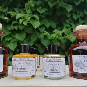 May include: Four small glass bottles with black lids and labels. The bottles contain a clear liquid and are labelled with the text "LV Apothecary" and the names of different scents: "Bergamot & Orange", "Lavender & Fennel", "Bergamot & Orange", and "Lavender & Fennel".