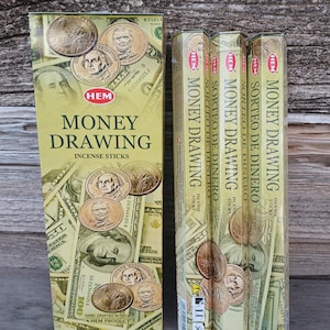 May include: A box and three packages of HEM Money Drawing incense sticks. The packaging features images of US currency and coins. The box reads "Money Drawing Incense Sticks" in green and gold lettering. The packages read "Sorteo de Dinero" in Spanish.