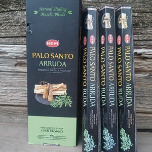 May include: A black box and three smaller boxes of HEM Palo Santo Arruda premium masala incense. The boxes feature text and images of incense sticks and leaves. The large box reads "Natural Healing Masala Blends".
