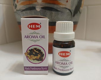 May include: A small brown glass bottle with a white cap, labeled "HEM Aroma Oil Mystic Frankincense Myrrh". The bottle is sitting on a white surface next to a white box with the same label.