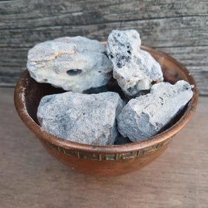 May include: A small copper bowl filled with gray and white stones. The stones are rough and have a natural texture.
