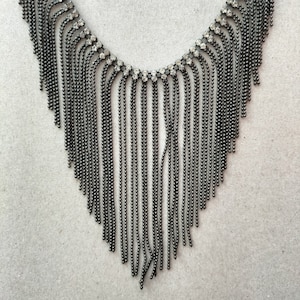 May include: A silver necklace with a fringe of chains and a row of clear rhinestones.