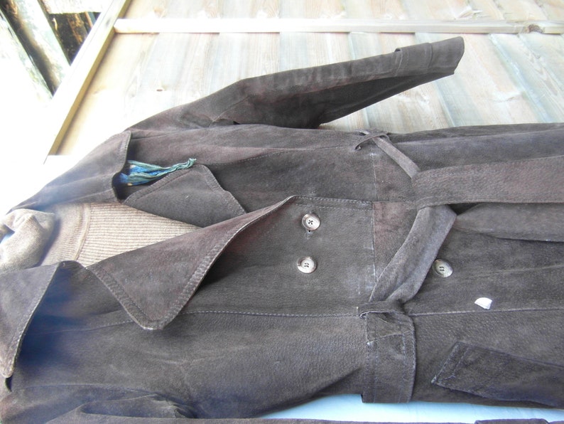 May include: A brown suede jacket with a long, flowing design. The jacket has a large collar, a belt, and two buttons on the front.