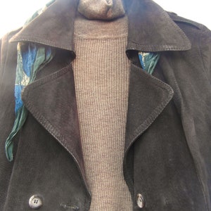 May include: A brown suede jacket with a brown turtleneck sweater and a blue and green patterned scarf. The jacket has two buttons on the front.