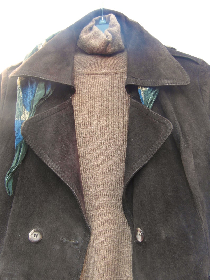 May include: A brown suede jacket with a brown turtleneck sweater and a blue and green patterned scarf. The jacket has two buttons on the front.