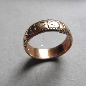 May include: A gold-colored band ring with a decorative pattern of stars and a beaded edge.