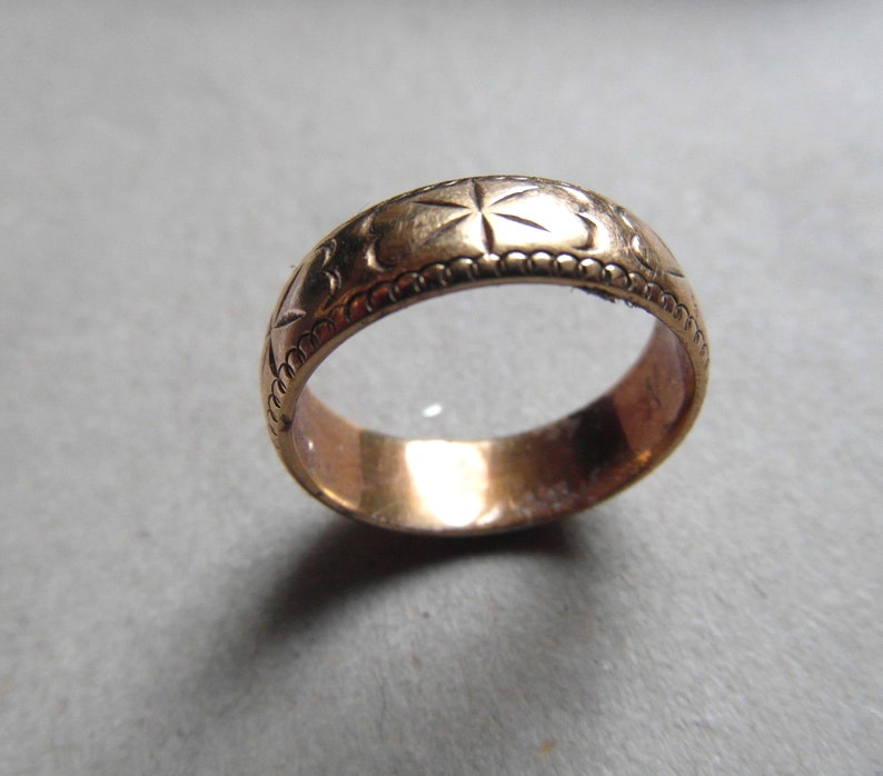 May include: A gold-colored band ring with a decorative pattern of stars and a beaded edge.
