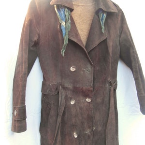 May include: A brown suede trench coat with a double breasted closure and a belt. The coat has a patterned scarf around the collar.