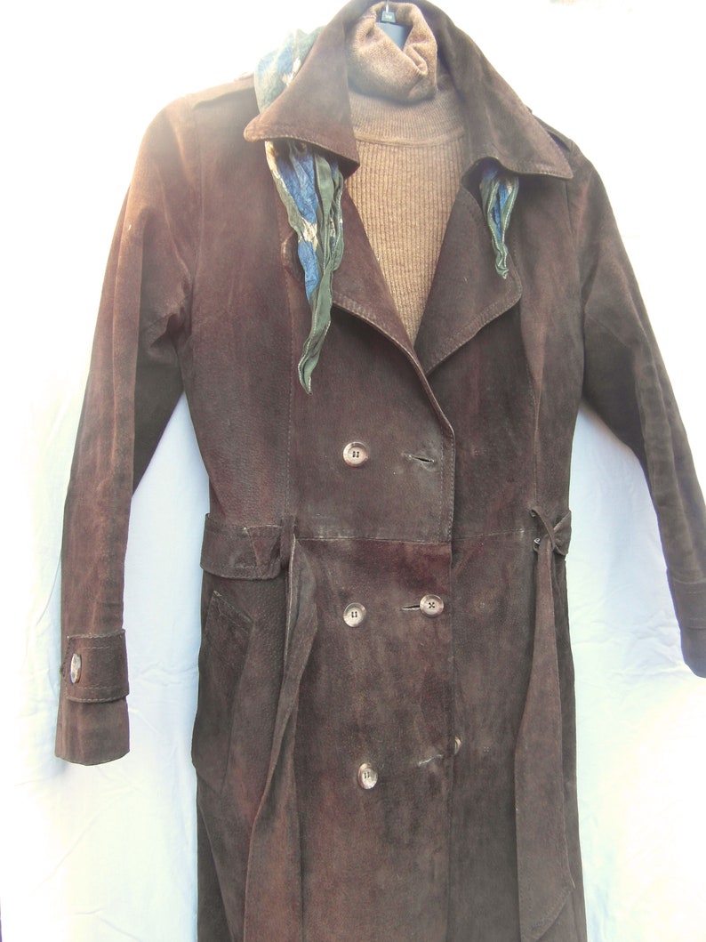 May include: A brown suede trench coat with a double breasted closure and a belt. The coat has a patterned scarf around the collar.
