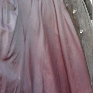 May include: A brown suede coat with a burgundy lining. The coat has a button closure and a collar.