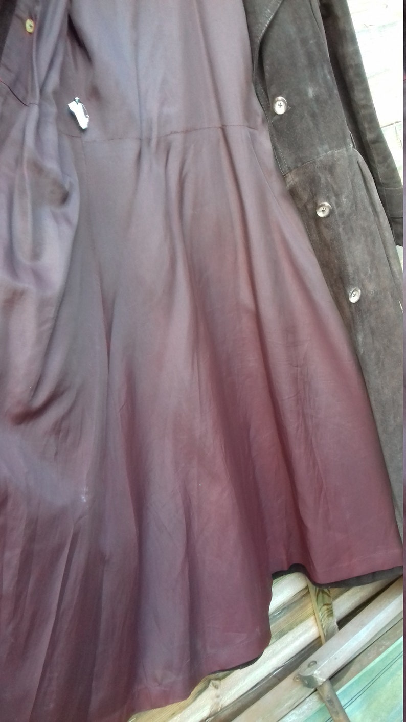 May include: A brown suede coat with a burgundy lining. The coat has a button closure and a collar.