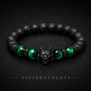 May include: A beaded bracelet featuring black porous lava stone beads, four smooth green tiger eye beads, and a central black metal wolf head charm with green eyes. The text ZIZIBRACELETS is printed in green at the bottom of the image.