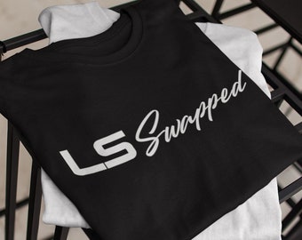May include: A black t-shirt with a white graphic that says "LS Swapped". The shirt is folded and displayed on a black metal rack.