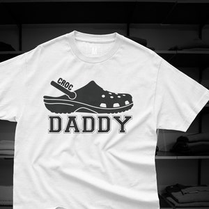 Könnte beinhalten: Weißes T-Shirt mit einer schwarzen Grafik eines Croc-Schuhs und dem Text "CROC DADDY".
