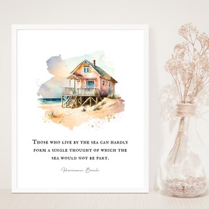 May include: Watercolor painting of a pink beach house on a sandy beach with a quote by Hermann Broch: "Those who live by the sea can hardly form a single thought of which the sea would not be part."