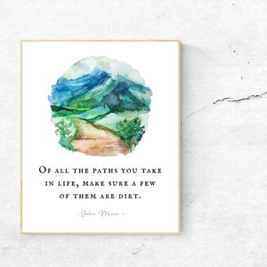 May include: A framed art print featuring a watercolor painting of a mountain scene in shades of blue and green. The print includes the quote, "Of all the paths you take in life, make sure a few of them are dirt."