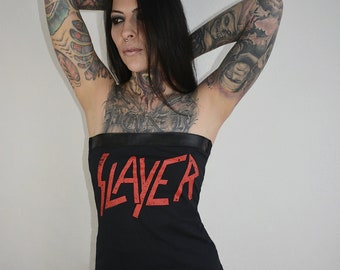 May include: A black strapless tube top featuring the word SLAYER printed in a distressed red font across the chest. The garment has a smooth black band along the top edge and is constructed from a solid black fabric, providing a fitted silhouette.