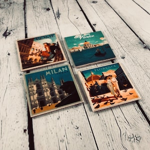 May include: Four square coasters with vintage travel posters featuring iconic landmarks from Italy. The coasters feature images of Rome, Venice, Milan, and Florence. Each coaster has a blue background with white text and a colorful image of a famous landmark.