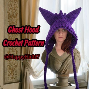 Puede incluir: Una capucha de fantasma de ganchillo morada con orejas puntiagudas y largas trenzas. El texto "Ghost Hood Crochet Pattern" se muestra en rojo. También es visible el identificador de la tienda de Etsy "@HappyKit327".