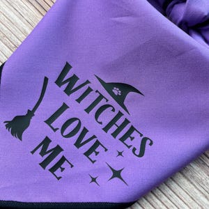 May include: Purple bandana with black text that reads "Witches Love Me" and a black silhouette of a witch's hat with a paw print on it.
