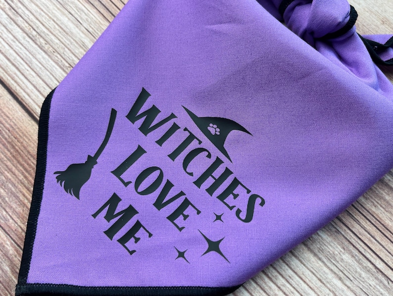 May include: Purple bandana with black text that reads "Witches Love Me" and a black silhouette of a witch's hat with a paw print on it.