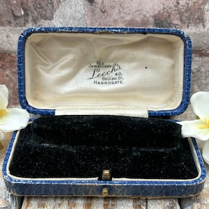 May include: A blue velvet jewelry box with a black velvet interior. The box has a brass latch and the inscription "The Jewellers Leech's, 40, Beulah St., Harrogate."