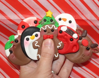 Könnte beinhalten: Eine Sammlung von Weihnachtsornamenten aus Ton, darunter ein Lebkuchenmann, ein Pinguin, ein Schneemann, ein Weihnachtsbaum, ein Rentier und Stechpalmen. Die Ornamente sind in verschiedenen Farben gehalten und vor einem rot-weiß gestreiften Hintergrund.