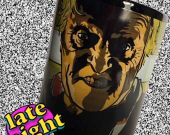 May include: Black ceramic mug with a graphic of a man's face with a menacing expression. The man has blonde hair and a beard. The mug has the text "late night" in pink and yellow letters.