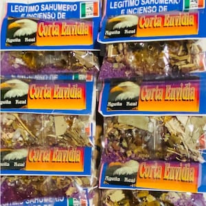 Puede incluir: Bolsas de incienso con la inscripción "Corta Envidia" en naranja y azul. Cada bolsa presenta un gráfico de un águila y las palabras "Aguila Real". Las bolsas contienen hierbas y flores secas.