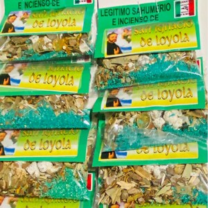Puede incluir: Una pila de pequeños paquetes verdes y blancos que contienen hierbas y flores secas. Los paquetes están etiquetados "Legitimo Sahumerio e Incienso de San Ignacio de Loyola".