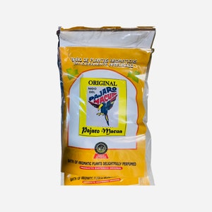 Puede incluir: Una bolsa de plástico transparente que contiene una bolsa amarilla con texto y una ilustración de un pájaro. La bolsa dice "ORIGINAL NIDO DEL PAJARO MACUA" y "BATH OF AROMATIC PLANTS DELIGHTFULLY PERFUMED".