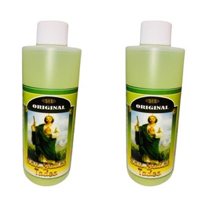 May include: Two clear glass bottles with yellow liquid and a green label featuring a religious image of a man holding a staff. The label reads "ORIGINAL" and "San Judas Tadeo".