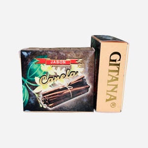 May include: A box of Gitana brand cinnamon soap. The box is brown with a gold border and features a picture of cinnamon sticks and white flowers. The text "Jabon Canela" is printed on the box in red and gold.