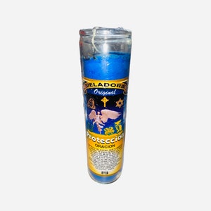 May include: Blue glass candle with a yellow label that reads "VELADORA Original" and "Protección ORACION". The label also features a white angel with wings, a cross, a star of David, a horseshoe, a four-leaf clover, and an owl.