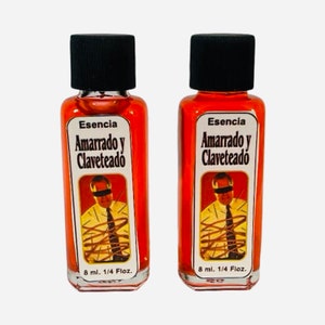 May include: Two small glass bottles with red liquid and black caps. The labels are white with black text that reads "Esencia Amarrado y Claveteado". Each bottle contains 8 ml or 1/4 fl oz of liquid.