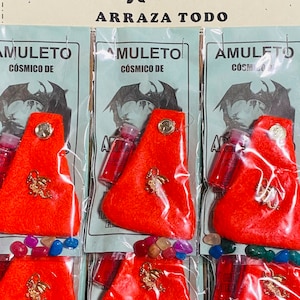 Puede incluir: Un conjunto de seis bolsitas rojas con dijes de dragón dorados, pequeñas botellas de líquido y piedras de colores. Las bolsitas están etiquetadas con "AMULETO COSMICO DE" y el empaque tiene el texto "TALISMAN MEJORADO PARA CORTAR TRABAJOS DE MAGIA NEGRA ARRAZA TODO".