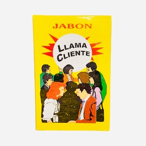 以下が含まれることがあります： 黄色い箱に「Jabon Llama Cliente」という文字が白い円の中に書かれており、その周りを赤い星が囲んでいます。箱には、人々のグループの漫画イラストが描かれています。